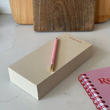 Notebook with a pink pen on a marble surface with wooden blocks in the background