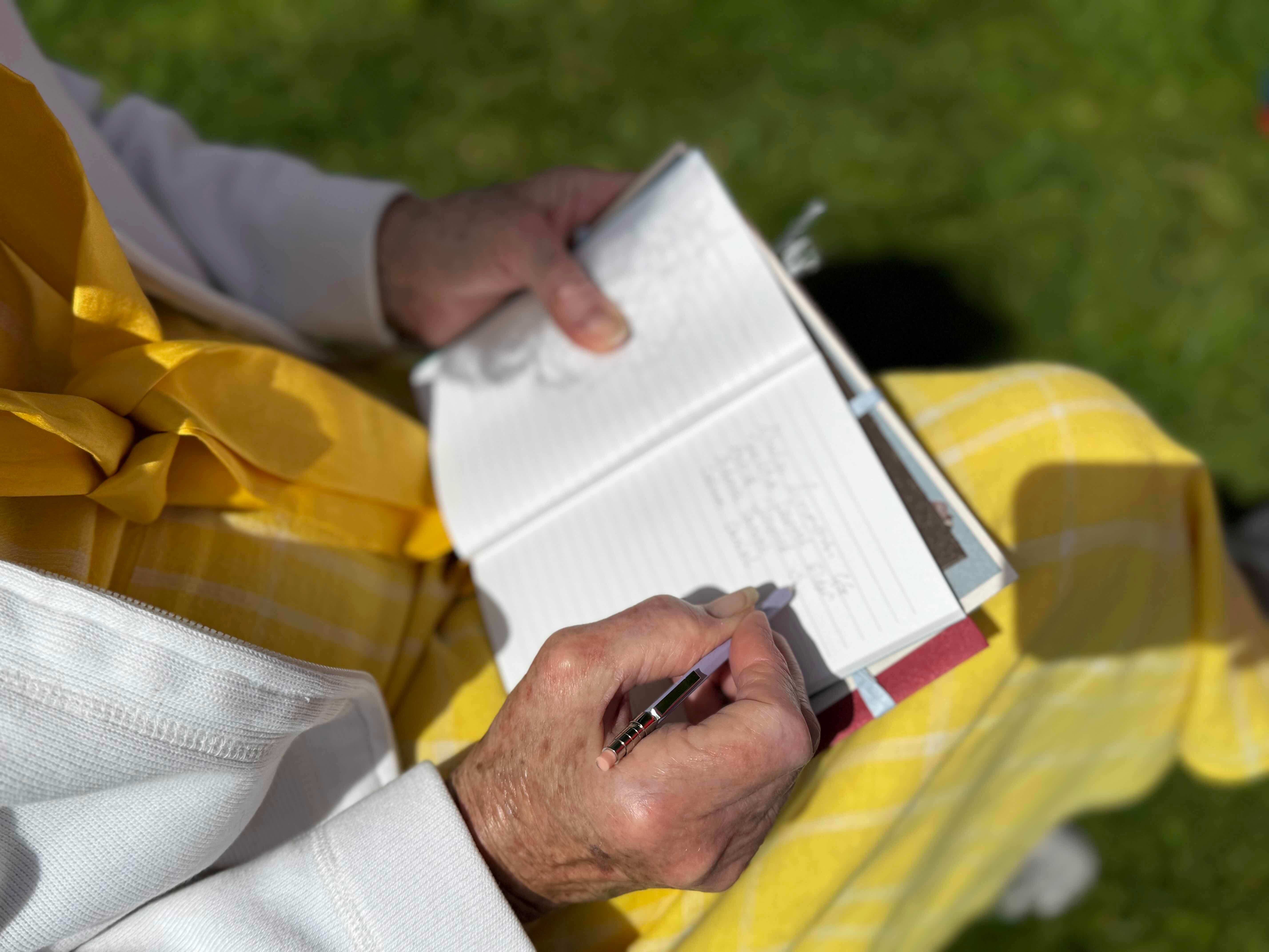 Person in a yellow and white outfit writing in a notebook outdoors.