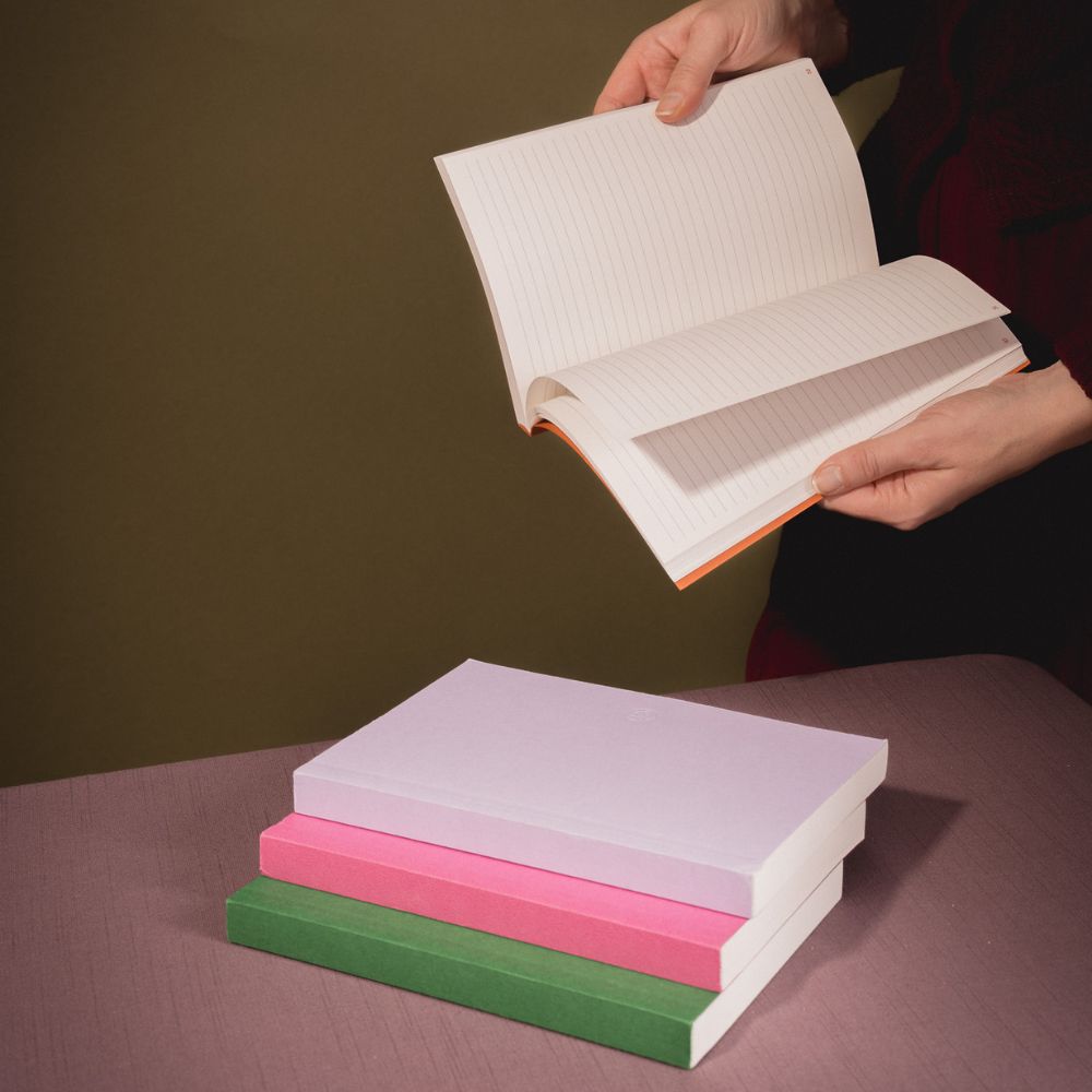 Open book held above a stack of colorful books on a table with a plain background