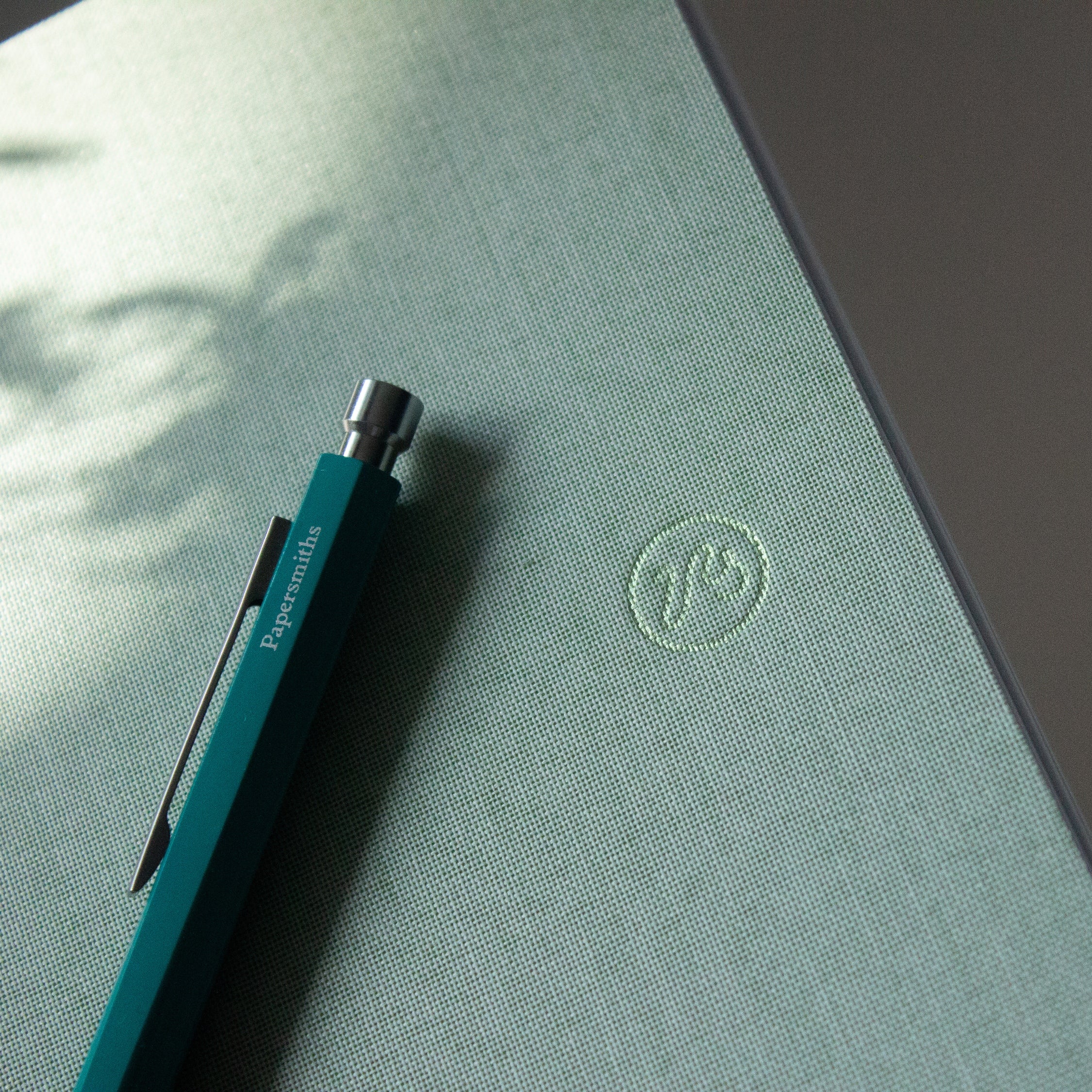 Blue pen on a green surface with a logo, on a blurred natural background