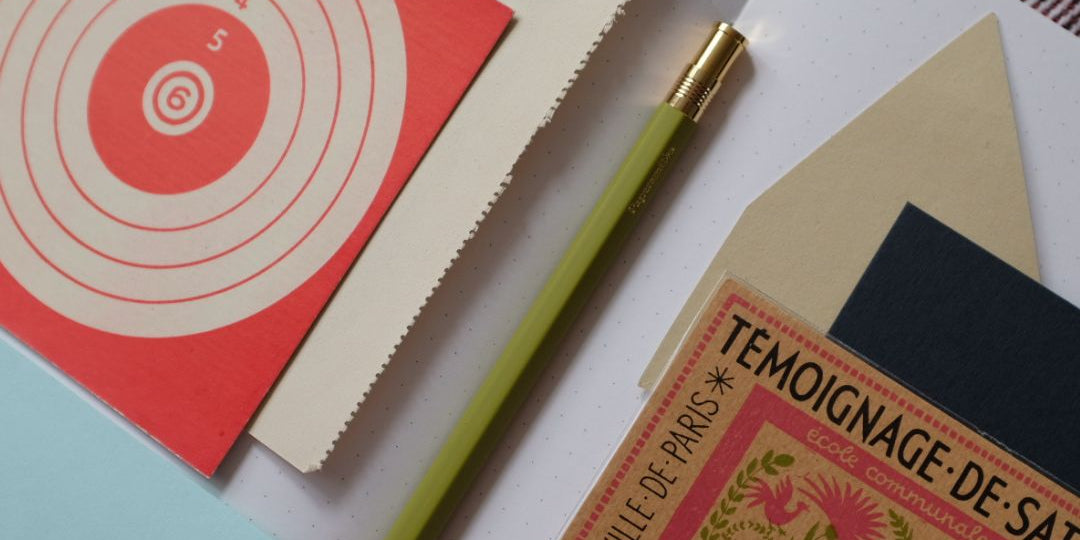 Collection of stationery items including a pen, notebooks, and a card with artistic design on a white surface.