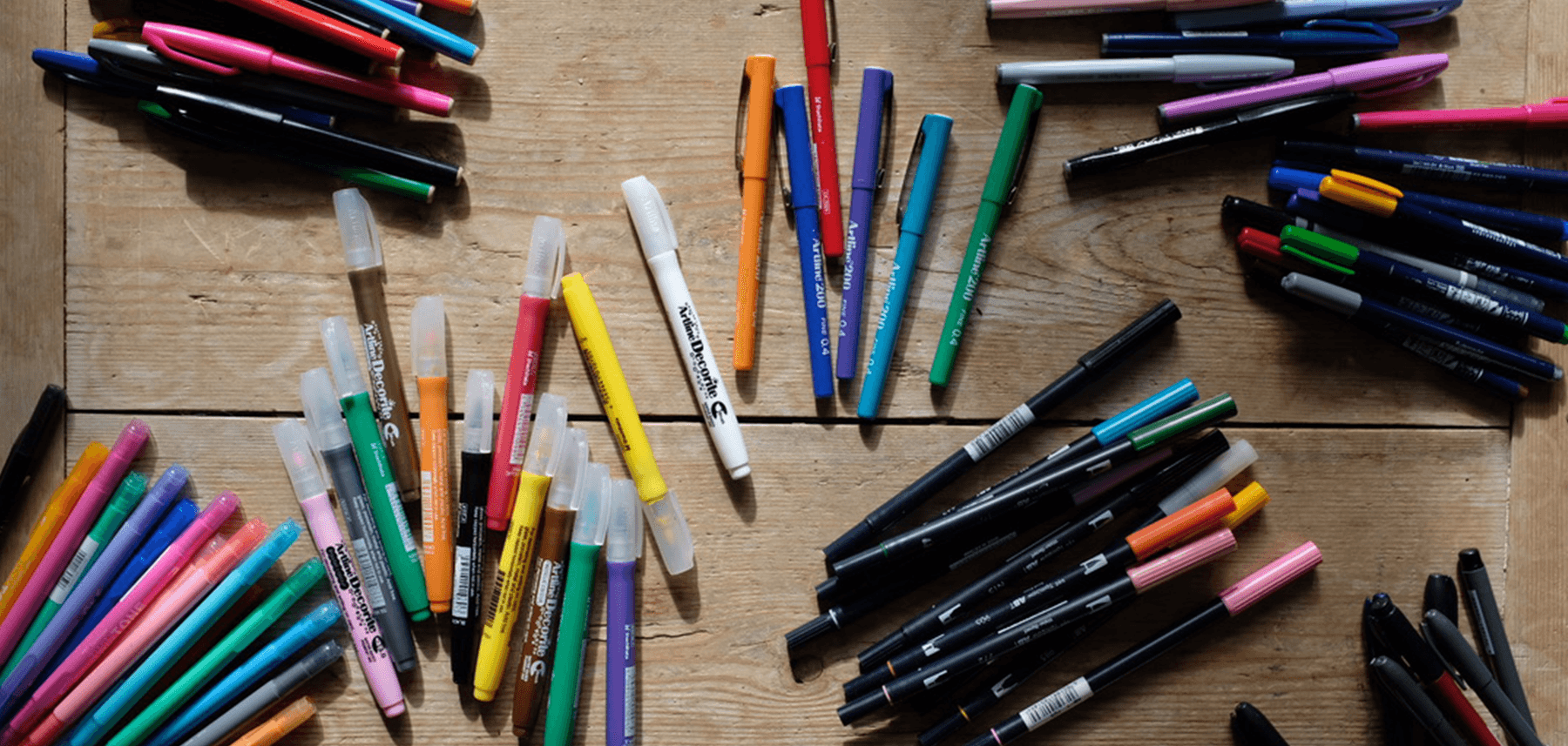 Assorted colorful markers and pens scattered on a wooden surface